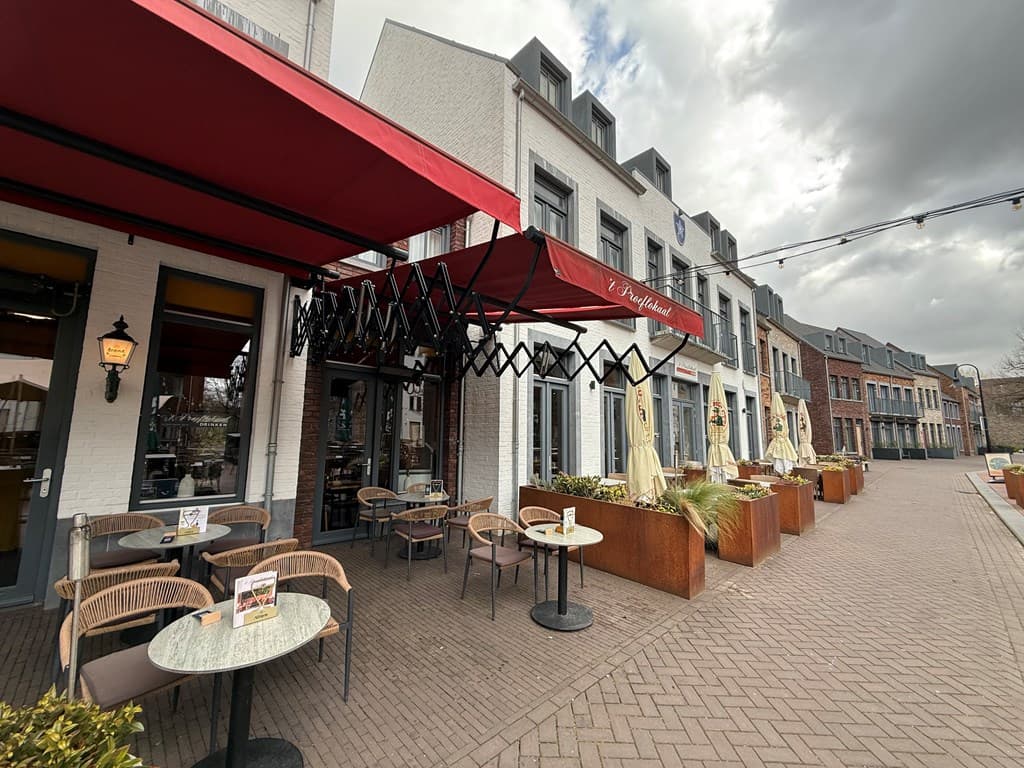 Terras van een restaurant met stoelen en tafels, omlijst door een vlakke promenade en gebouwen op de achtergrond