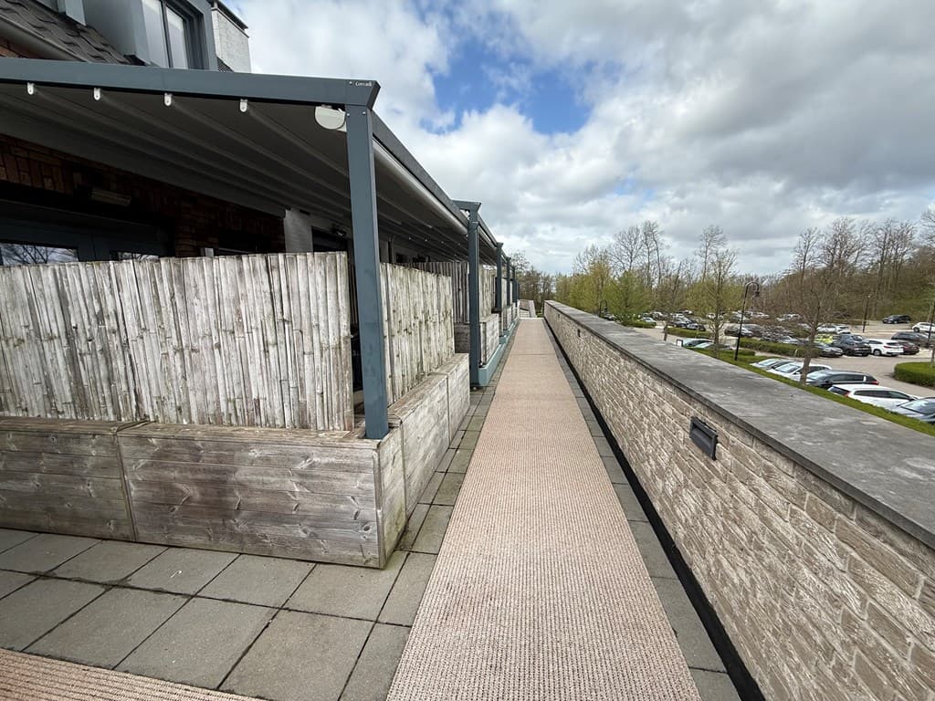 Aanleg van een pad met aan beide zijden houten hekken en uitzicht op groen en parkeerplaatsen in de afstand.