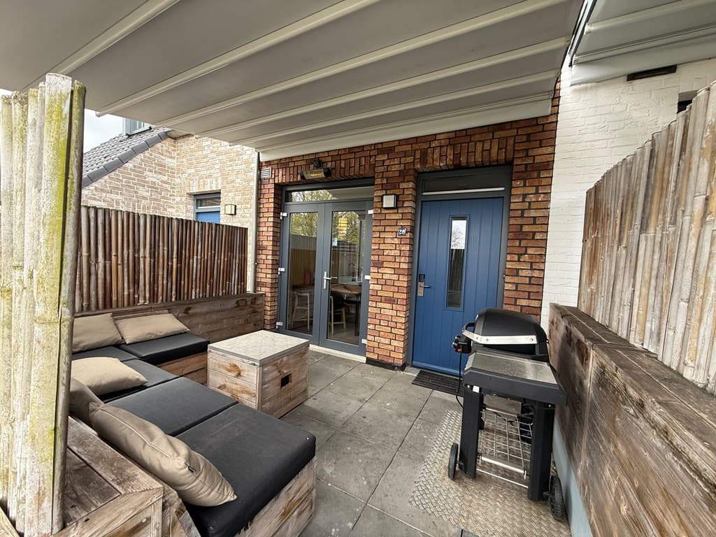 Terras met houten banken, kussen, een barbecue en dubbele deur naar de woning, achterom bij een stenen muur