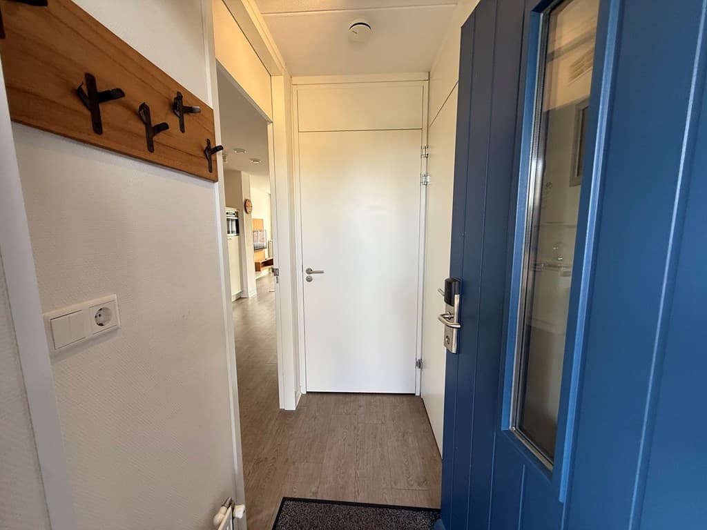 Entree met een blauwe deur, wandhaakjes aan de muur en een zicht op de binnenruimte van de woning