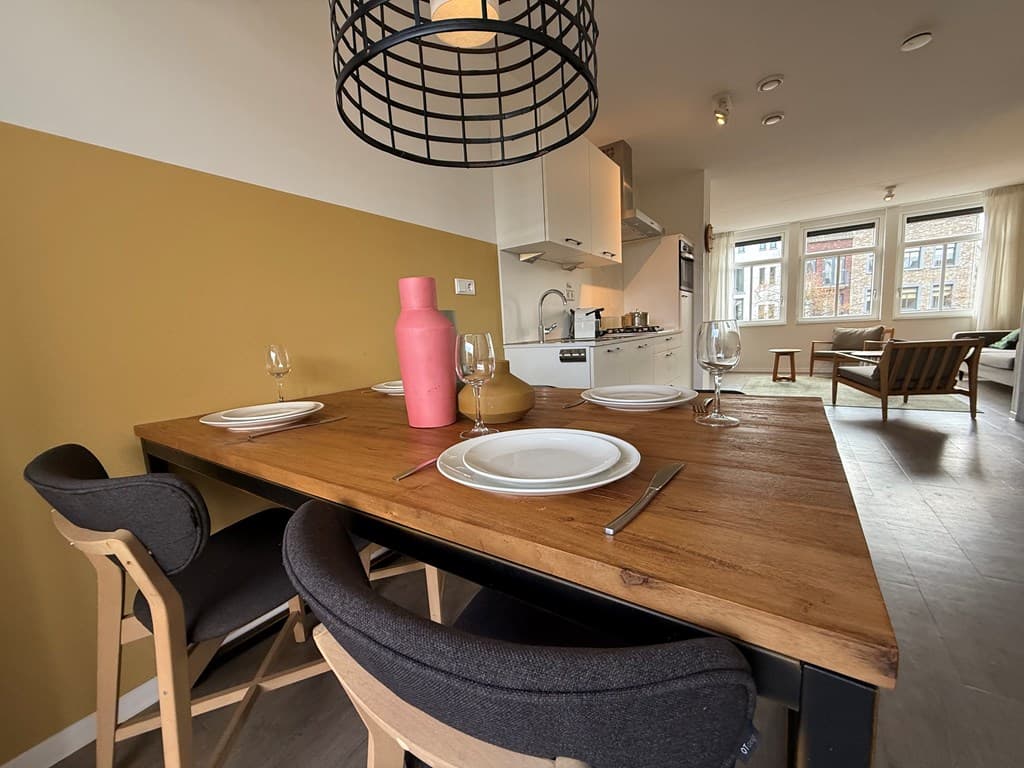 Eenvoudige eetruimte met een houten tafel, stoelen, servies en een moderne keuken op de achtergrond
