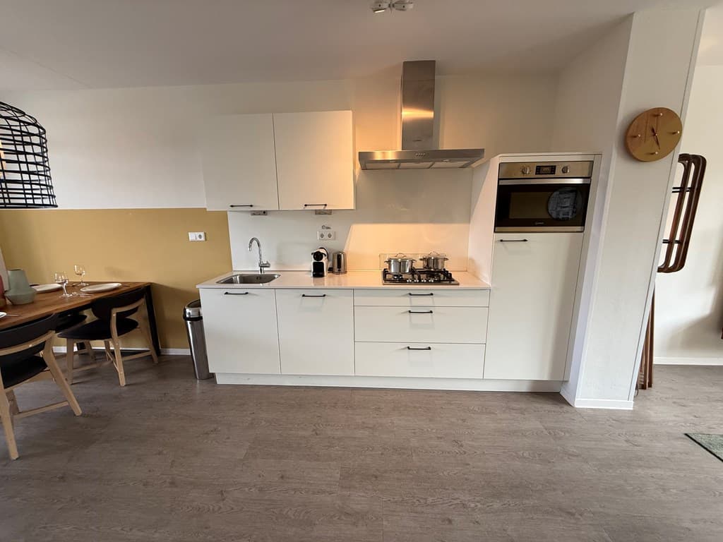 Keuken met moderne apparatuur, witte kasten en een eetgedeelte met houten tafel en zwarte stoelen.