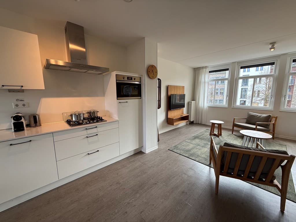 Moderne woonkamer met open keuken, zithoek en grote ramen voor natuurlijk licht.
