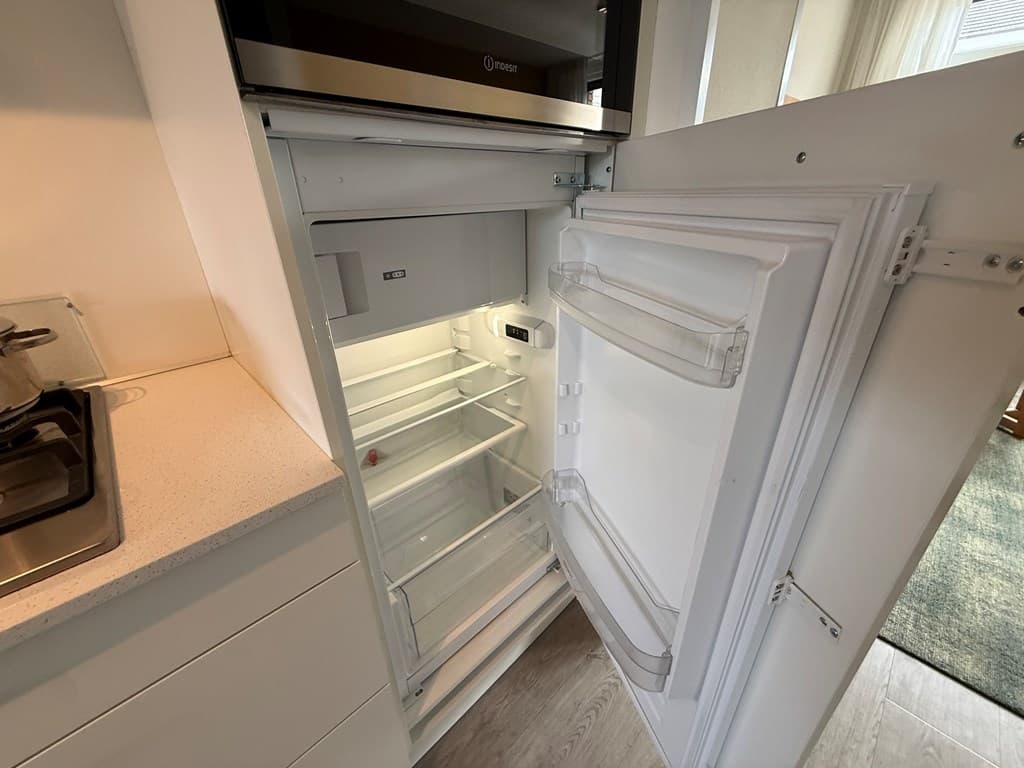 Open koelkast met enkele planken en een doorzichtige lade, geplaatst in een moderne keukenomgeving