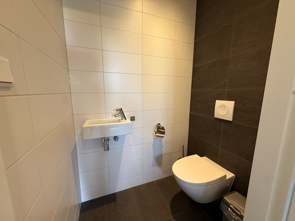 Wit betegeld toilet met wandcloset, fonteintje en handdoekhouder in een moderne ruimte