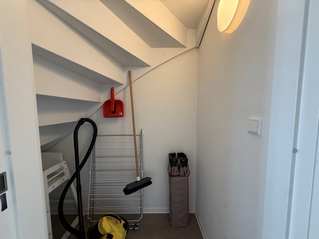 Berging onder de trap met schoonmaakspullen, een droogrek en een lampje aan de wand