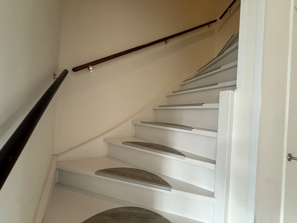 Lichte trap met houten leuning en witte treden in een woning.