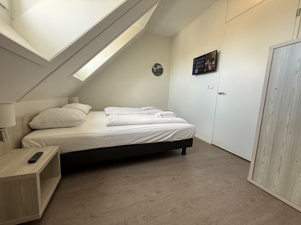 Slaapkamer met een tweepersoonsbed, kasten, nachtkastje en een tv aan de muur onder een schuin plafond