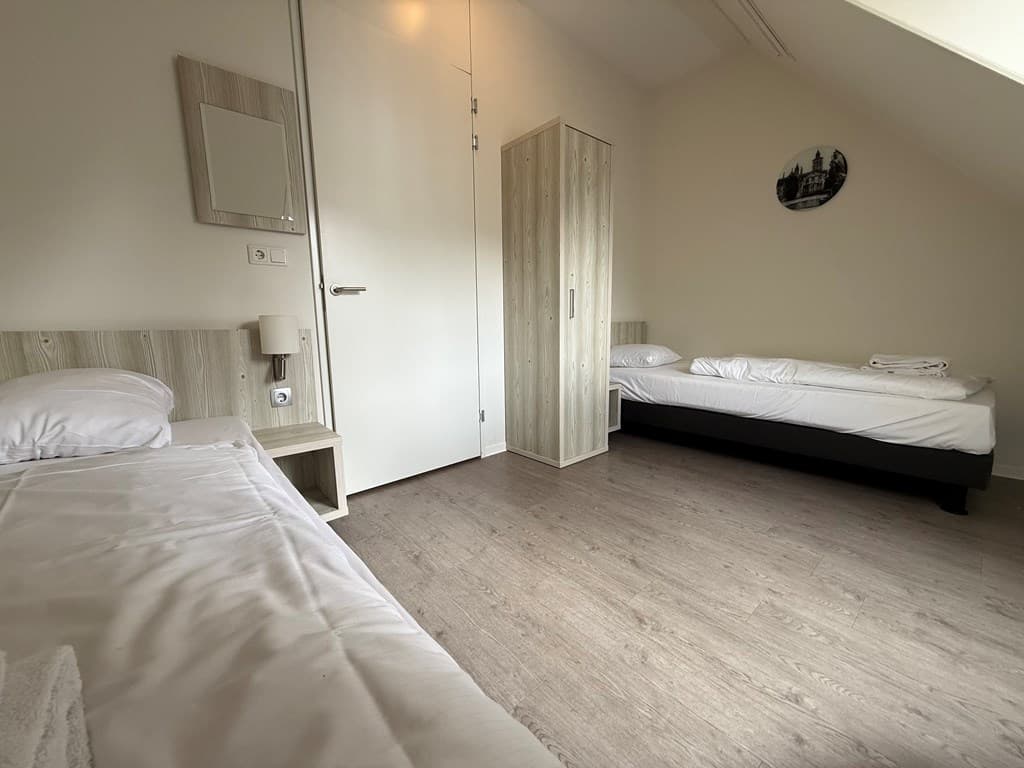 Slaapkamer met twee eenpersoonsbedden, kast, spiegel en moderne, lichte afwerking