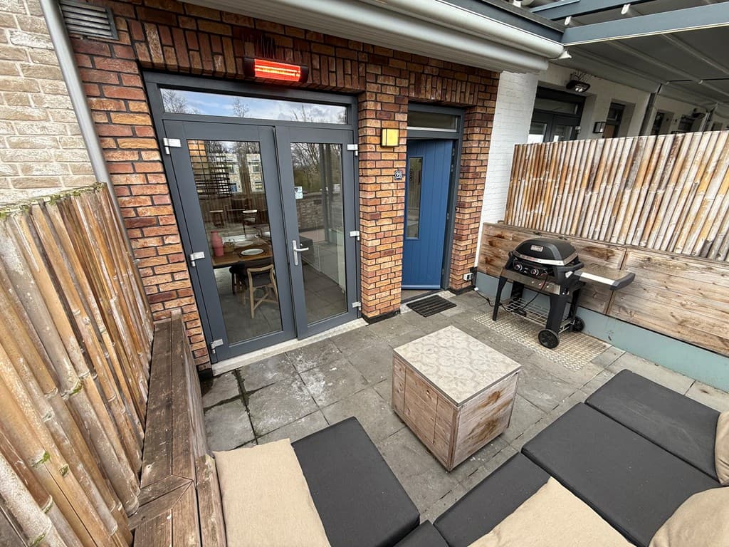 Terras met een houten schutting, zitgelegenheid, een barbecue en grote openslaande deuren naar binnen.