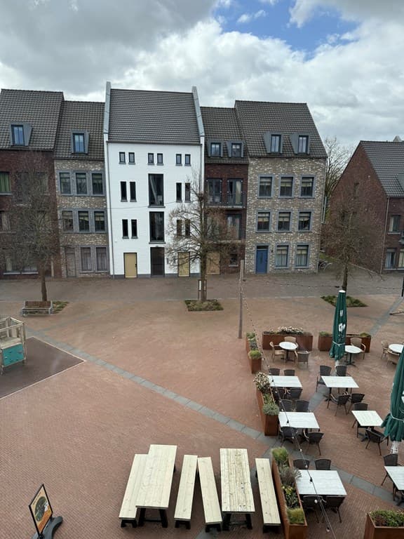 Geheel van appartementen met uitzicht op een plein en zitplaatsen met groene parasols en bloembakken.