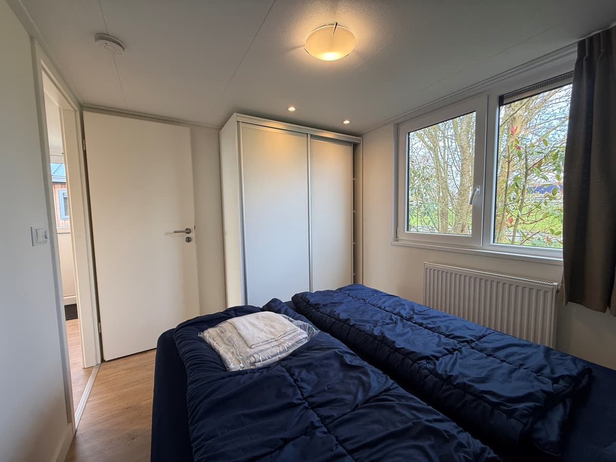 Slaapkamer met twee eenpersoonsbedden, een kast en ramen met zicht op groen buiten.