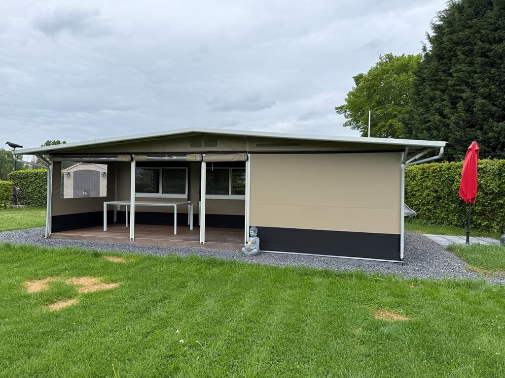 Buitenzijde van een woning met een overdekt terras, een grote tafel, en een parasol in de tuin met gazon.