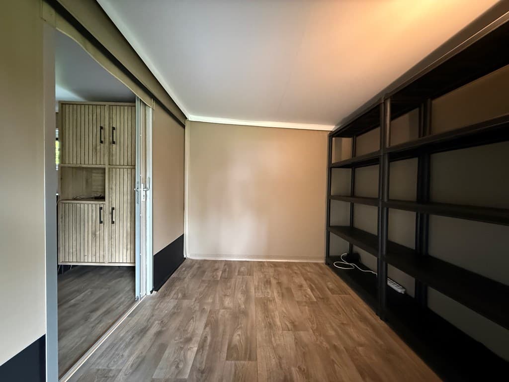 Binnenruimte met laminaatvloer, open kast of plankensysteem en een spiegelwand met toegang tot een andere ruimte.