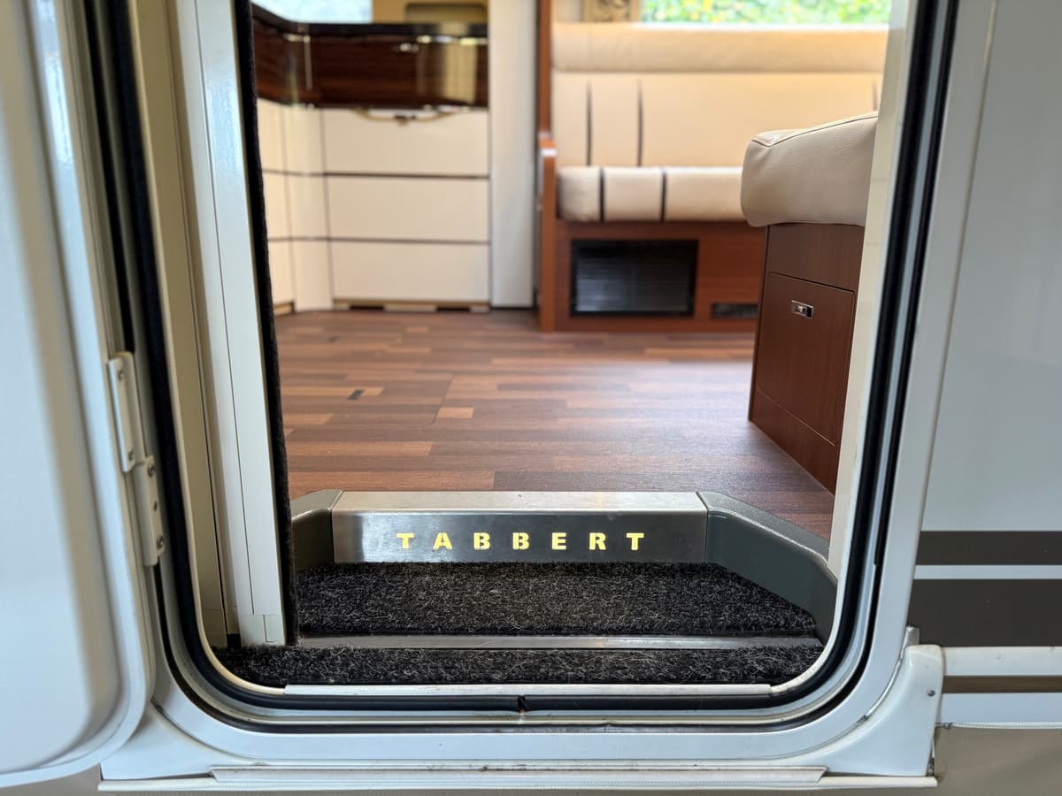 Ingang van een caravan met een tapijt bij de deur en de naam 'TABBERT' zichtbaar op de trede.