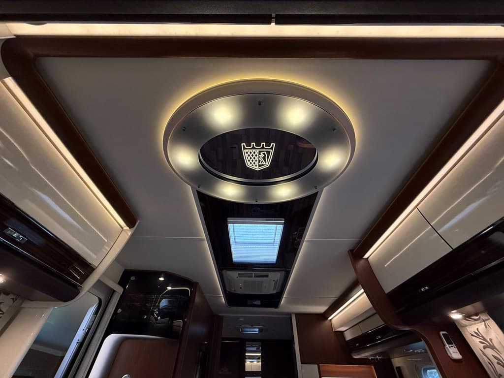 Plafond van een moderne woning met verlichting en een geïntegreerde ventilatierooster, voorzien van een merklogo in het midde