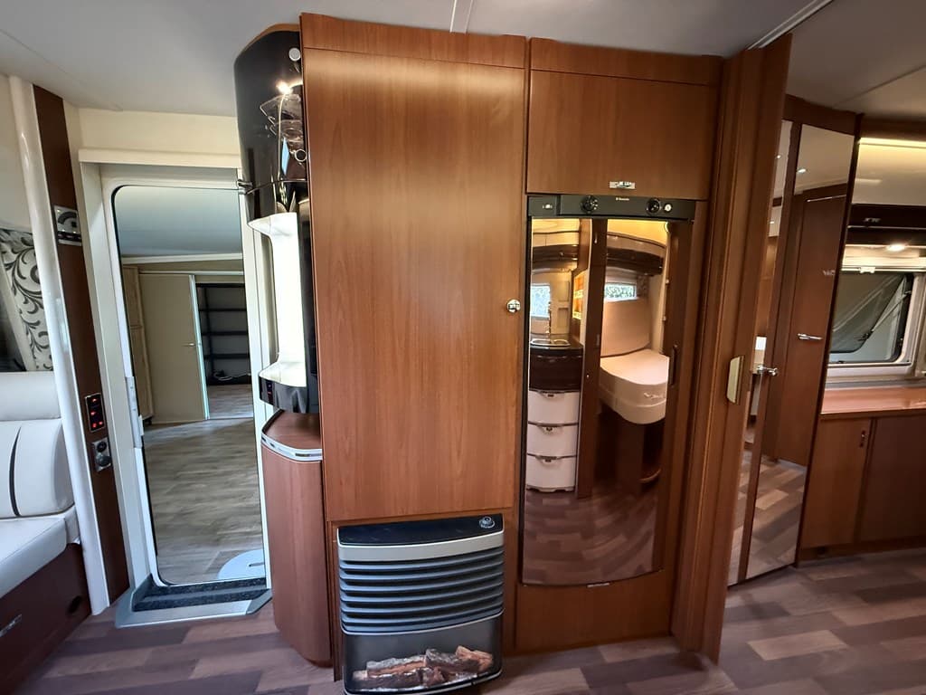 Interieur van de woning met een houten kast, koelkast, kachel en toegang naar een andere ruimte.