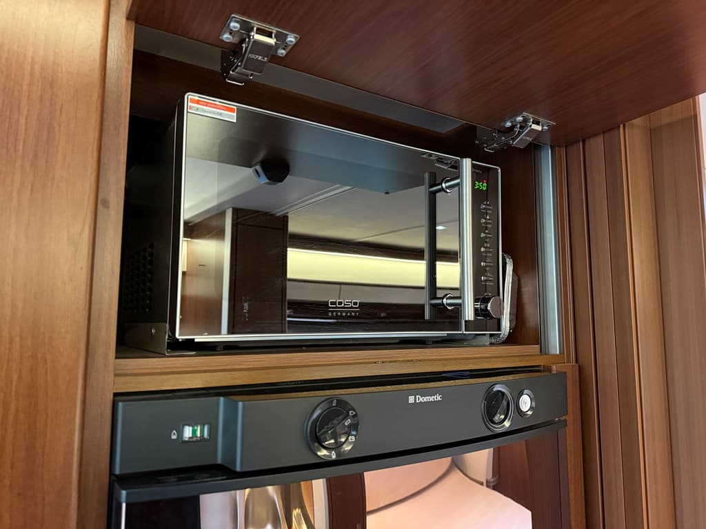 Moderne magnetron boven een koelkast in een houten keukenkast met verlichting en een strakke afwerking