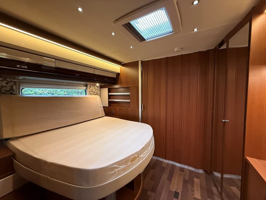 Slaapkamer met een rond bed, houten wanden en ingebouwde kasten, verlicht door plafondspots.