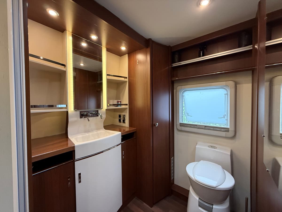 Moderne badkamer met een wastafel, spiegel, toilet en opbergruimte, gelegen bij een raam met uitzicht.