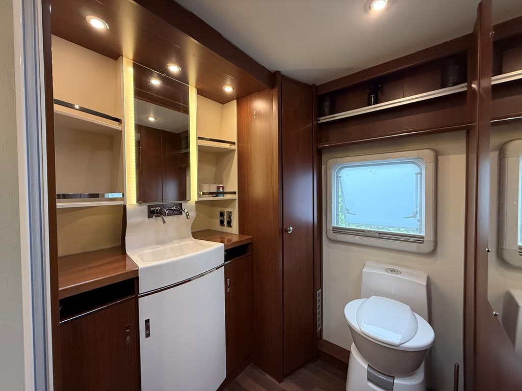 Moderne badkamer met een wastafel, spiegel, toilet en opbergruimte, gelegen bij een raam met uitzicht.