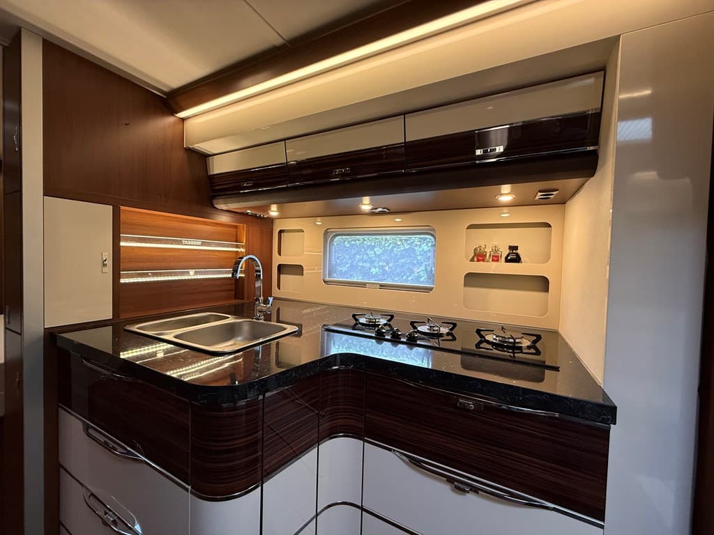 Moderne keuken met zwart aanrechtblad, gasfornuis en ingebouwde planken voor opbergruimte.