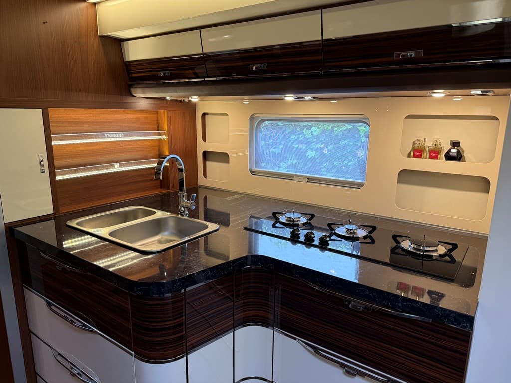 Moderne keuken met donker houten kasten, een zwart granieten werkblad, dubbele spoelbak en gaskookplaten.