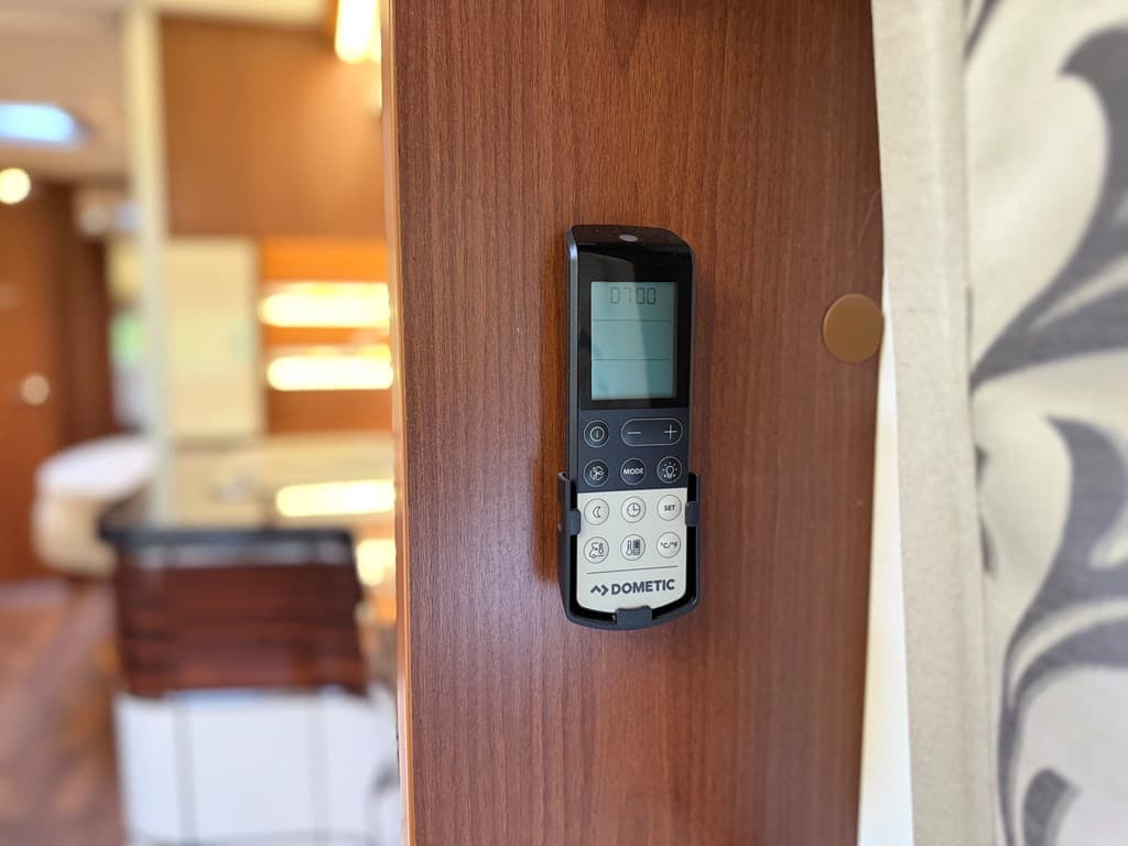 Afbeelding van een wand met een Dometic afstandsbediening bevestigd aan een houten paneel in een vakantiewoning.