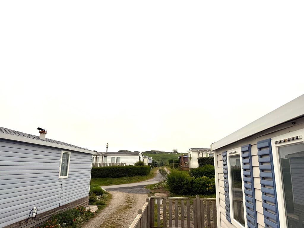 Uitzicht vanaf de woning met caravanhuizen en een grindpad tussen groene struiken en een heuvel in de verte.