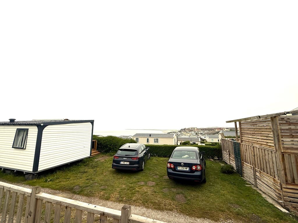 Twee geparkeerde auto’s naast een vakantiewoning met uitzicht op zee en een houten schutting in de achtergrond