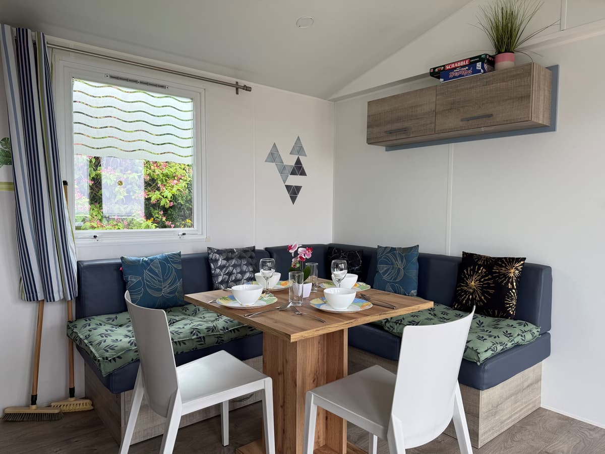 Eettafel met banken in een lichte kamer, verschillende kussens en planten op de plank aan de muur