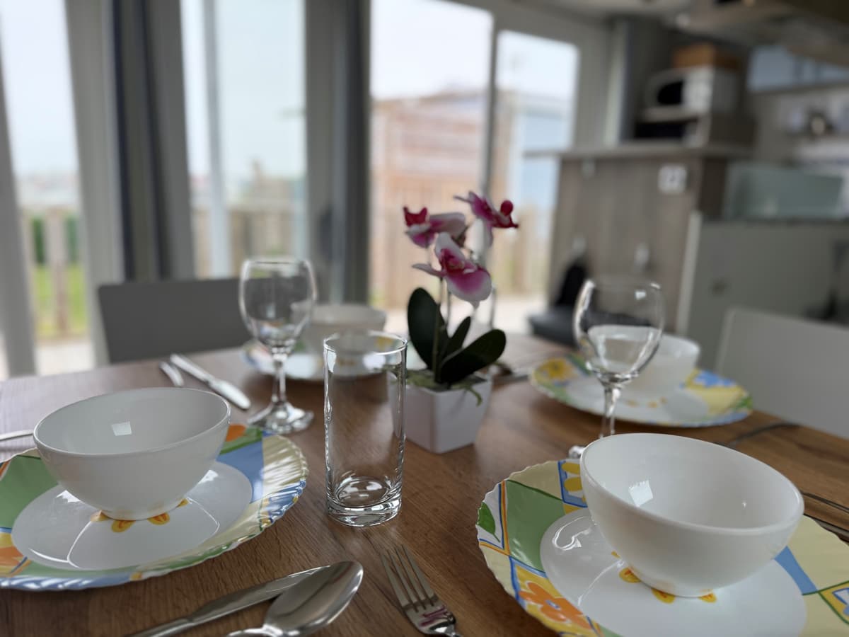 Eetkamertafel gedekt met servies en glazen, uitzicht op groene omgeving door raam op de achtergrond