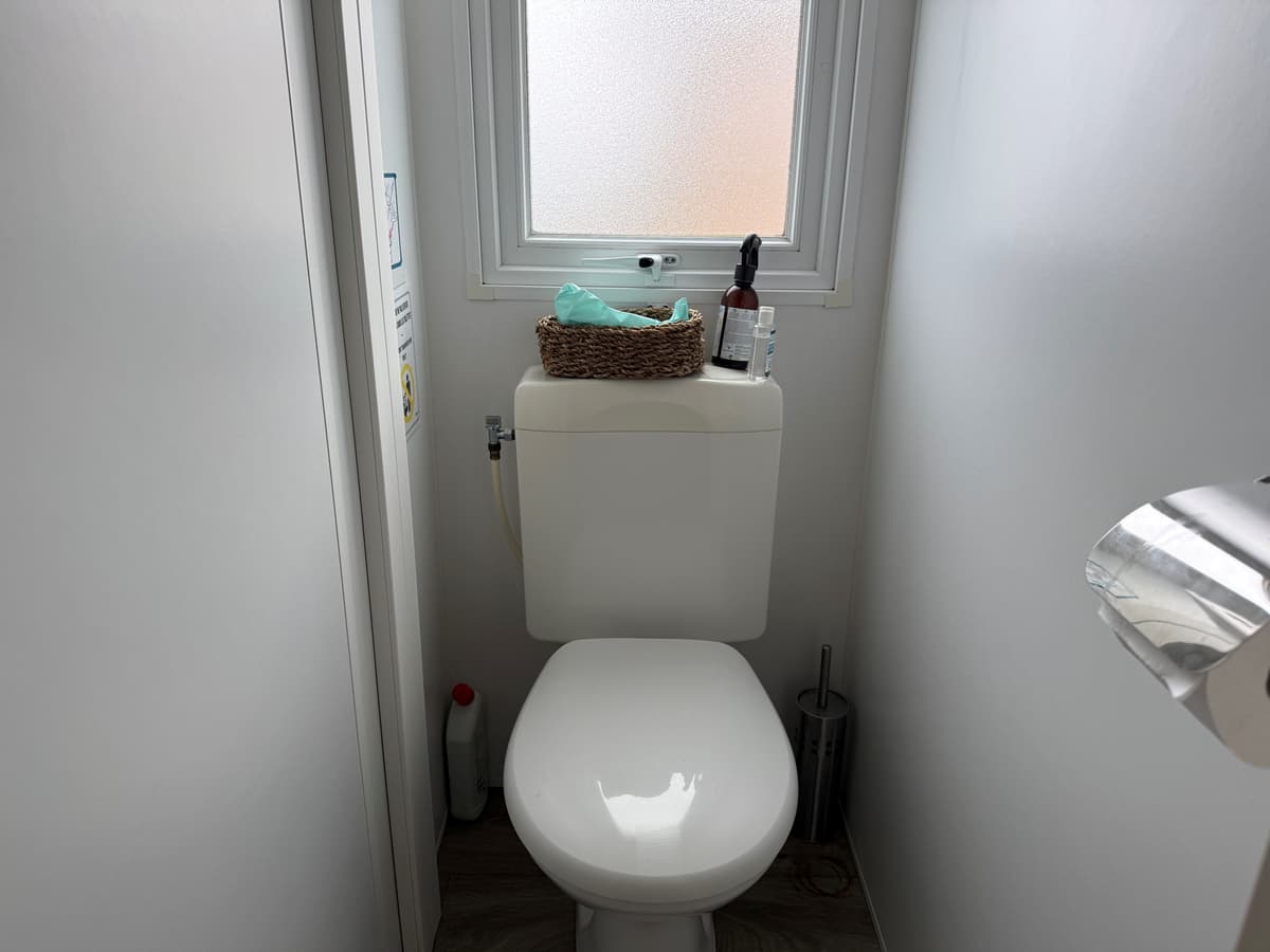 Toilet met staand sanitair, raam met gestructureerd glas en enkele accessoires op de toiletcistern.