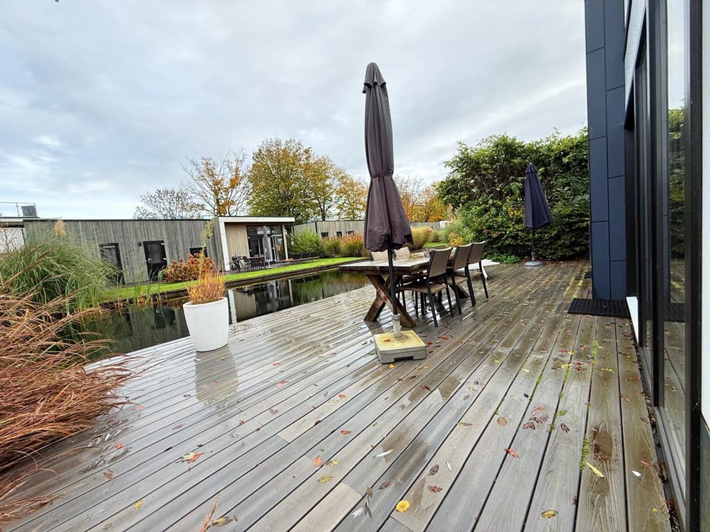 Houten terras met zitgelegenheid en parasol, uitzicht op een vijver en omringende begroeiing