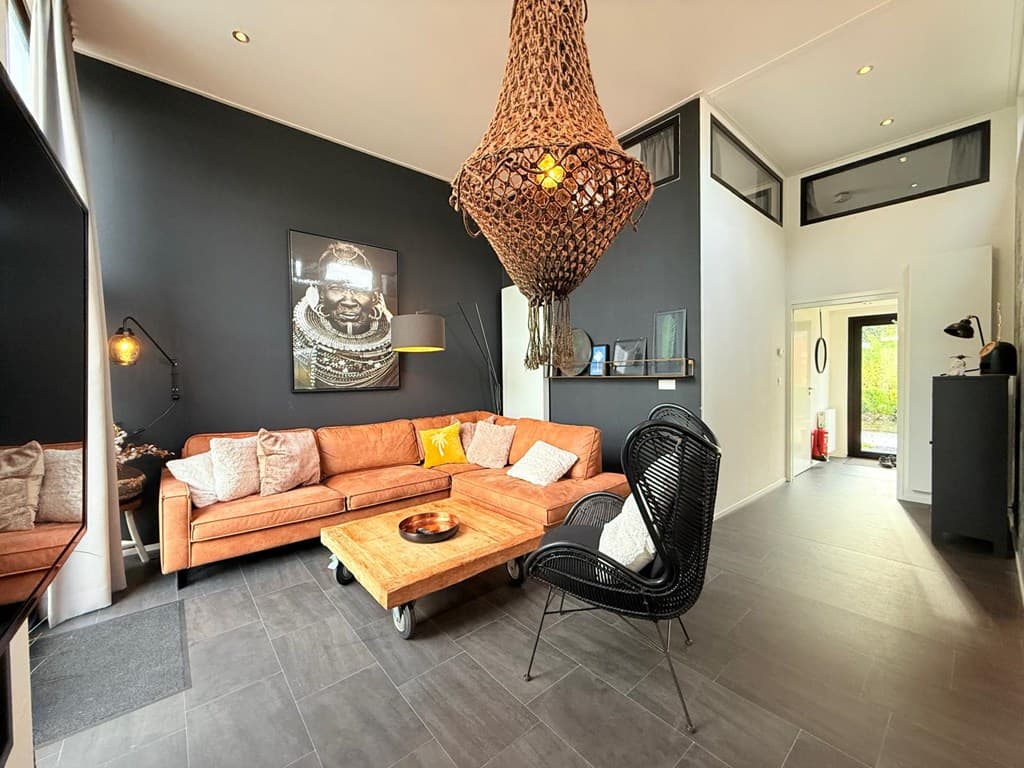 Ruime woonkamer met een leren bank, houten salontafel, kunst aan de muur en een unieke hanglamp.