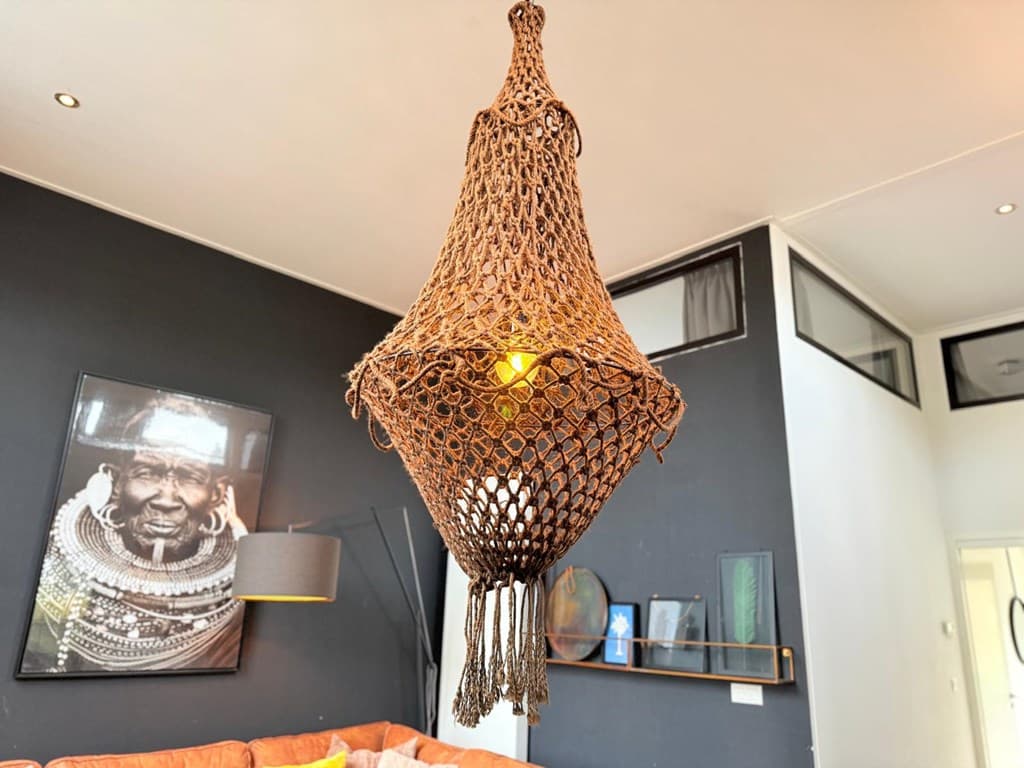Hanglamp van gevlochten materiaal met een warme gloed, achtergrond met een zwart-witte afbeelding en een moderne inrichting.