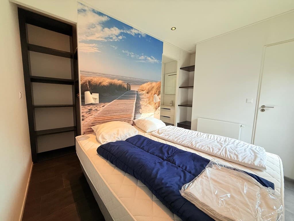 Slaapkamer met twee bedden, wanddecoratie van een strand en open opbergplanken bij de deur