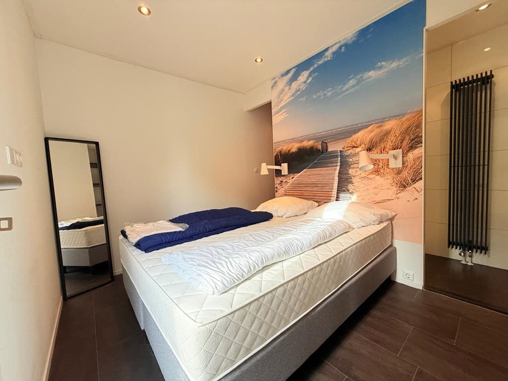 Slaapkamer met tweepersoonsbed, grote spiegel, wanddecoratie van een strand en een radiator in de hoek.