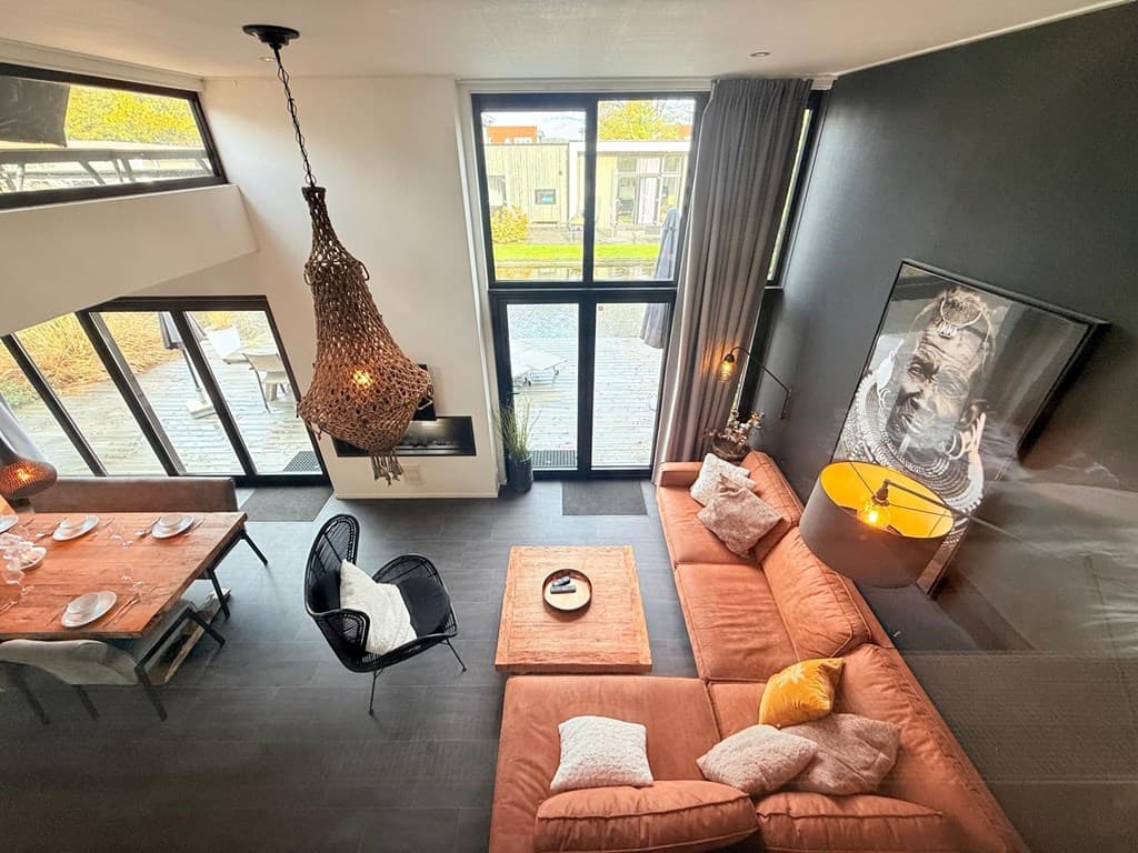 Moderne woonkamer met grote ramen, een bank, eettafel en opvallende lamp boven een tafel