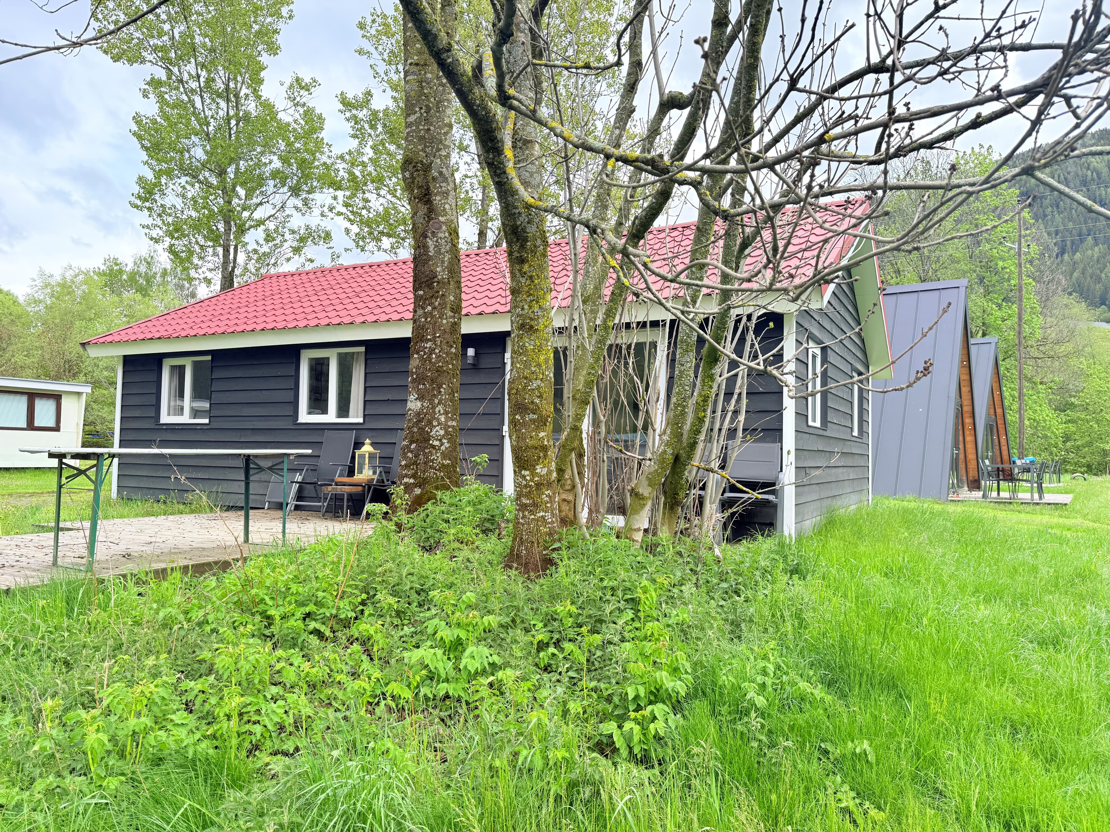 Houten woning met rode dak, omgeven door een grote groene tuin en meerdere bomen.
