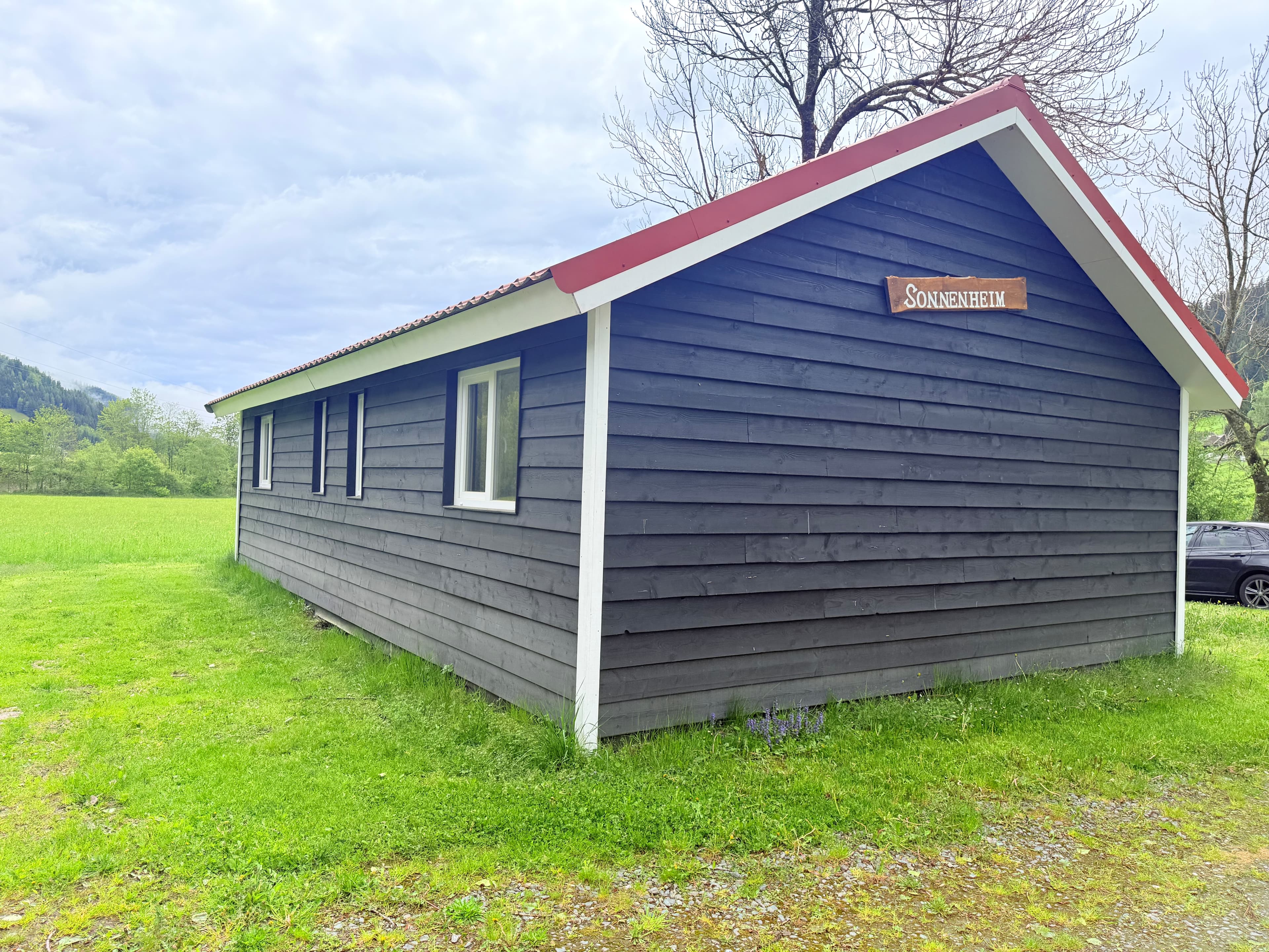 Zijaanzicht van een houten vakantiewoning met een rode dakrand en een bord met de naam Sonnleiten aan de gevel