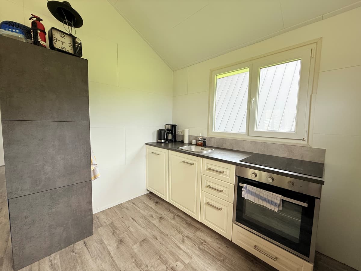 Keuken met moderne kasten, oven, aanrecht en raam met uitzicht op buiten.