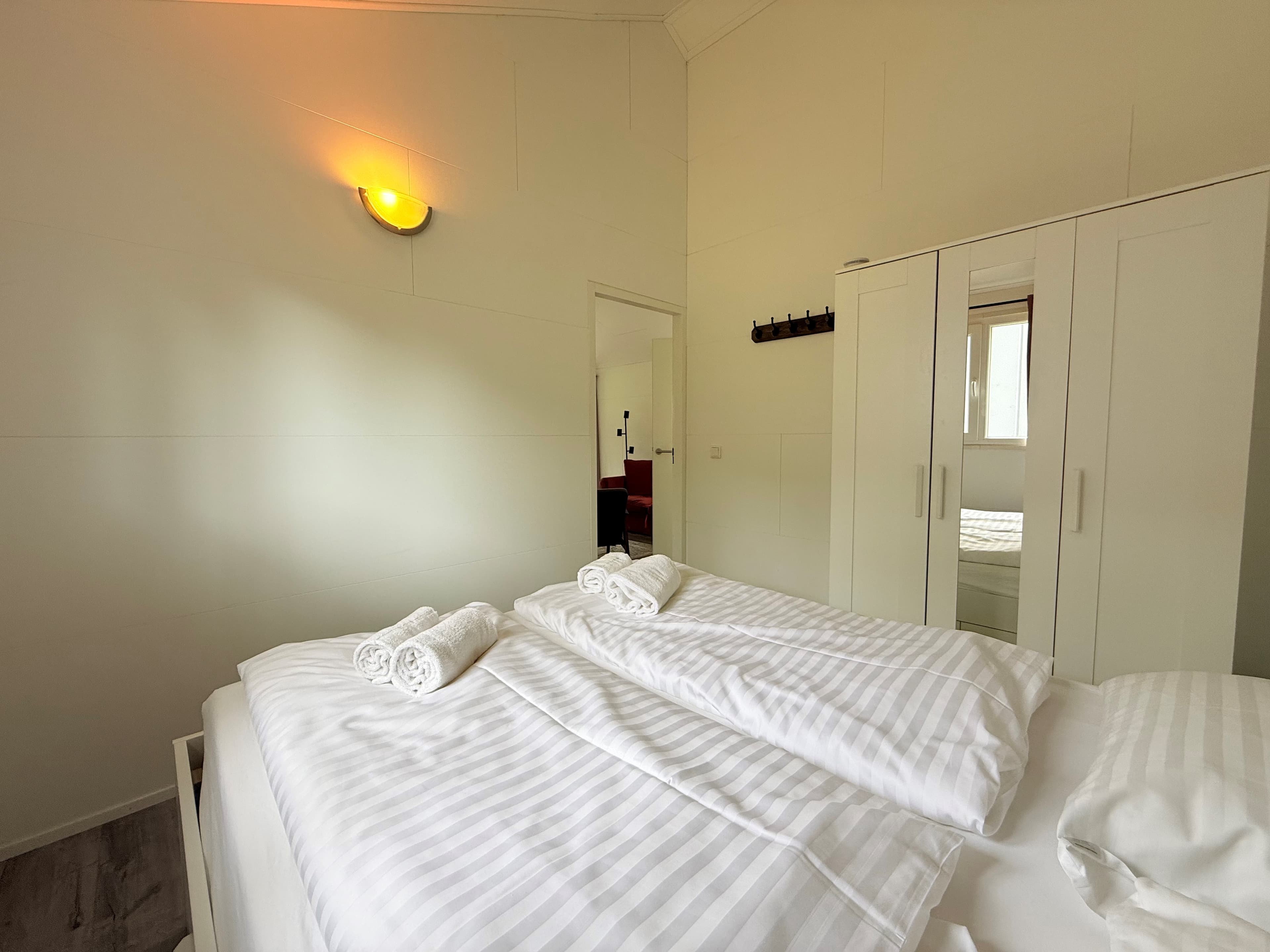 Hoofdslaapkamer met tweepersoonsbed, witte beddengoed en kasten in een lichte, neutrale ruimte