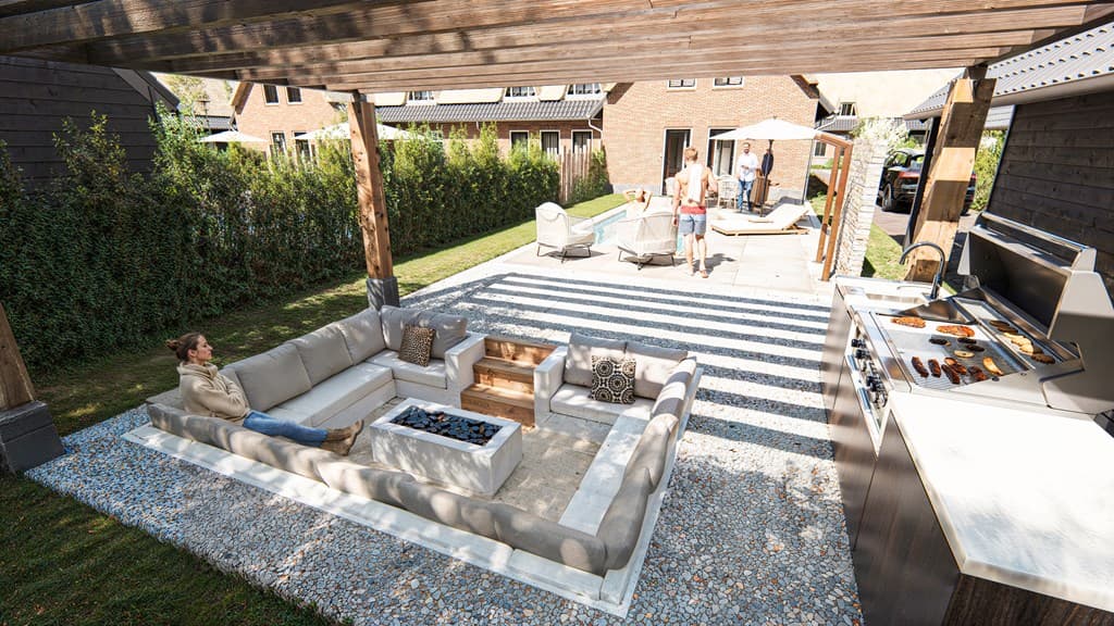 Overdekt terras met comfortabele zithoek, grill en uitzicht op de achtertuin met bestrating en loungeplek