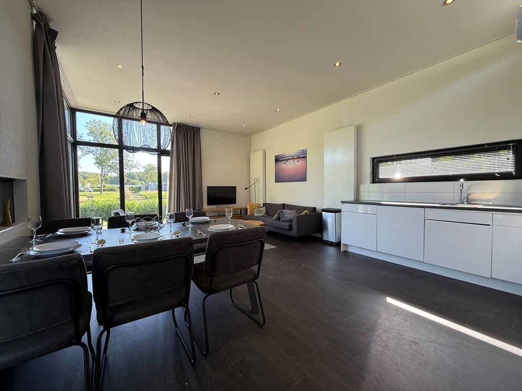 Moderne woonkamer met open keuken en eetruimte, grote ramen met uitzicht op groen buiten en minimalistische inrichting