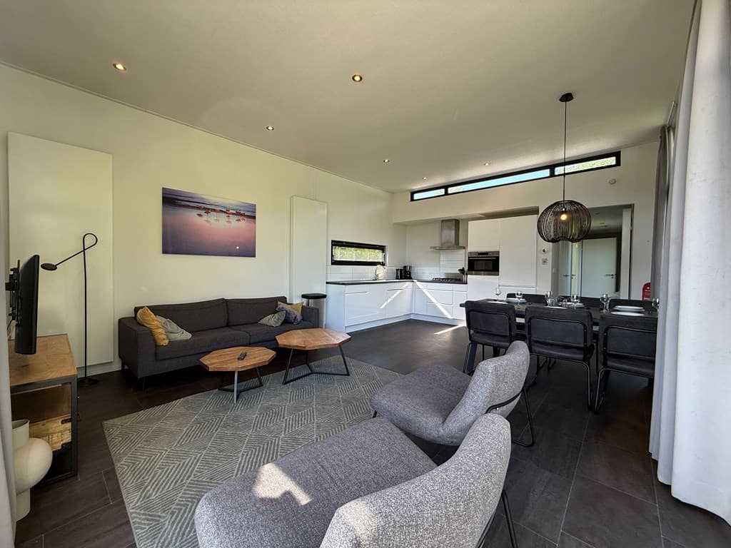 Gezellige woonkamer met zithoek en eetruimte, grote ramen en moderne keuken in EuroParcs Spaarnwoude.