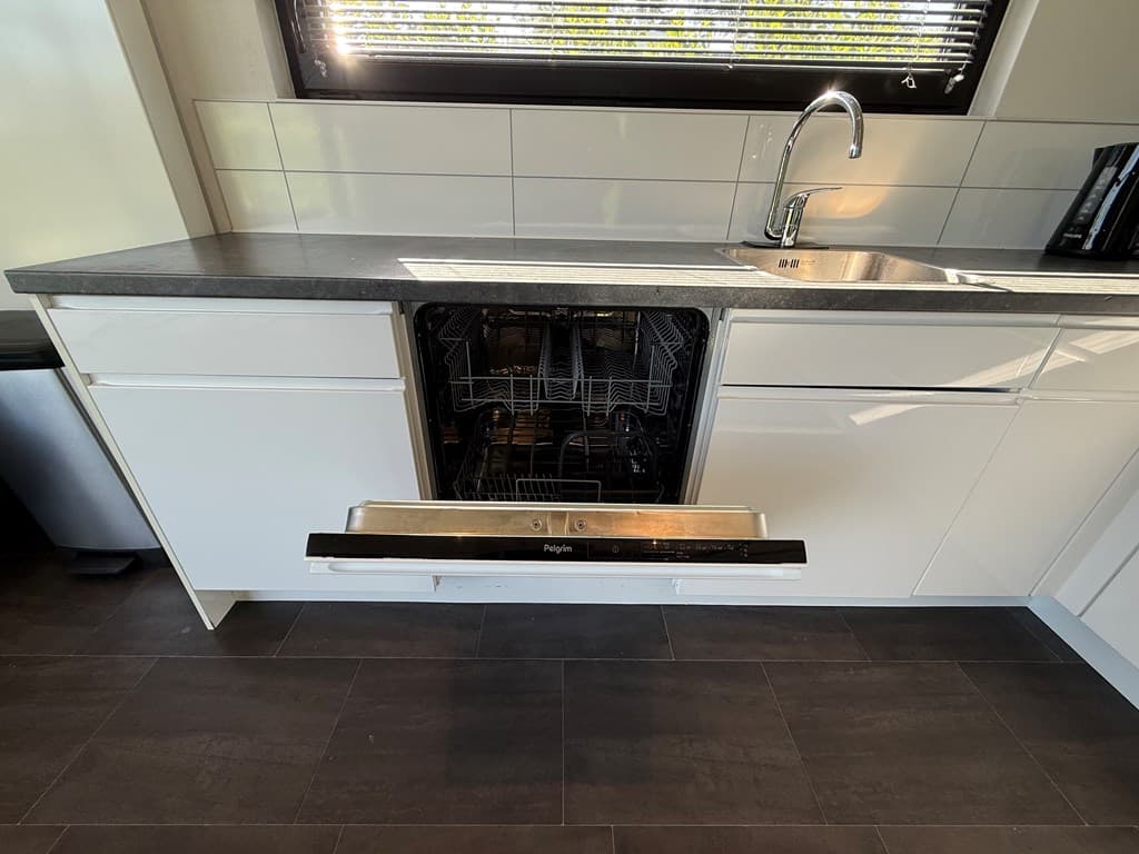 Moderne keuken met een open vaatwasser in een witte keukenkast en een aanrecht van donkergrijs materiaal.