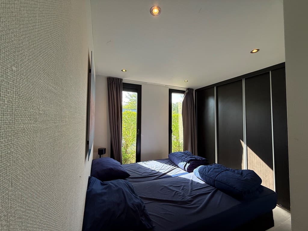 Slaapkamer met twee eenpersoonsbedden en grote ramen met uitzicht op groen.