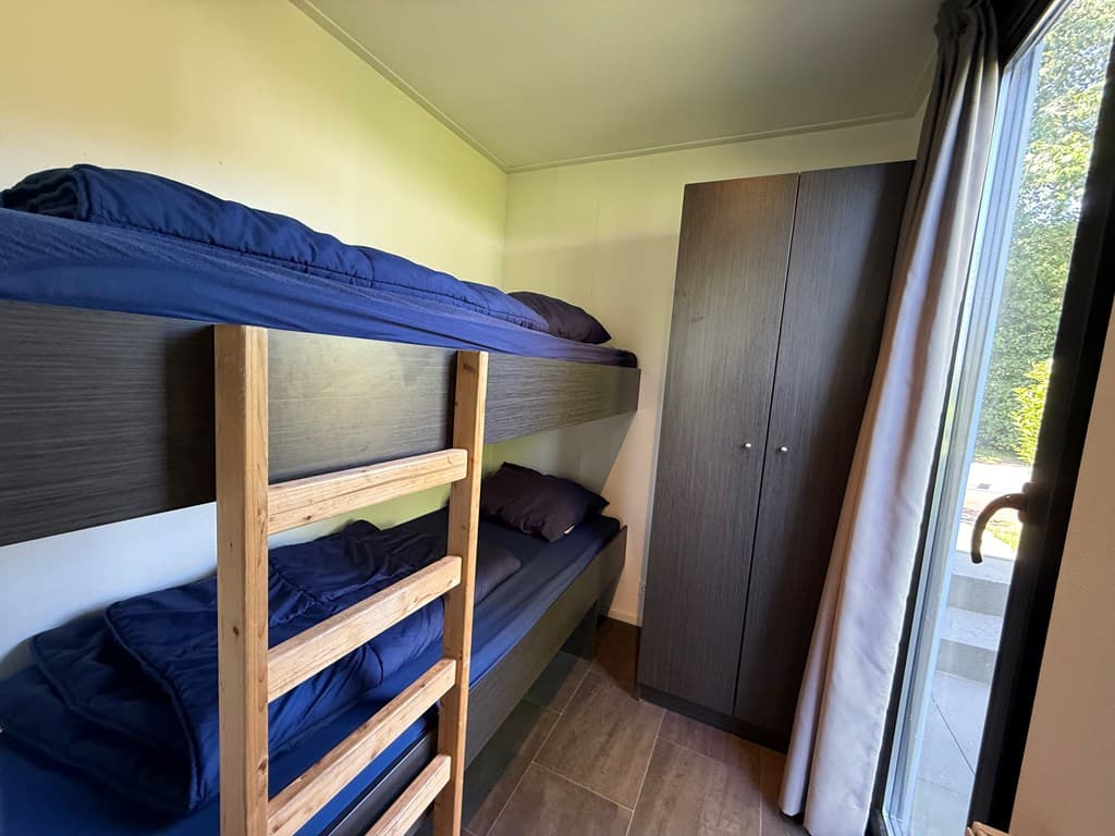 Slaapkamer met stapelbed en kast, lichtinval via een grote raampartij naar buiten.