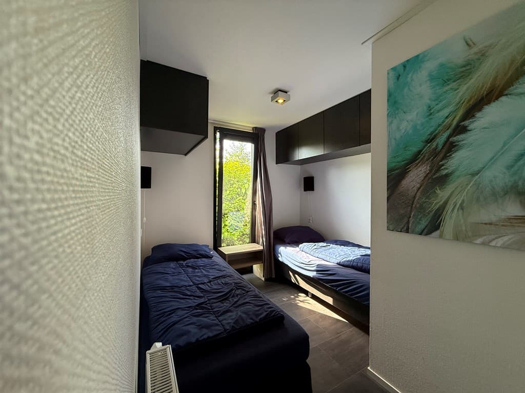 Slaapkamer met twee eenpersoonsbedden, ramen met uitzicht op groen en wandplanken boven de bedden